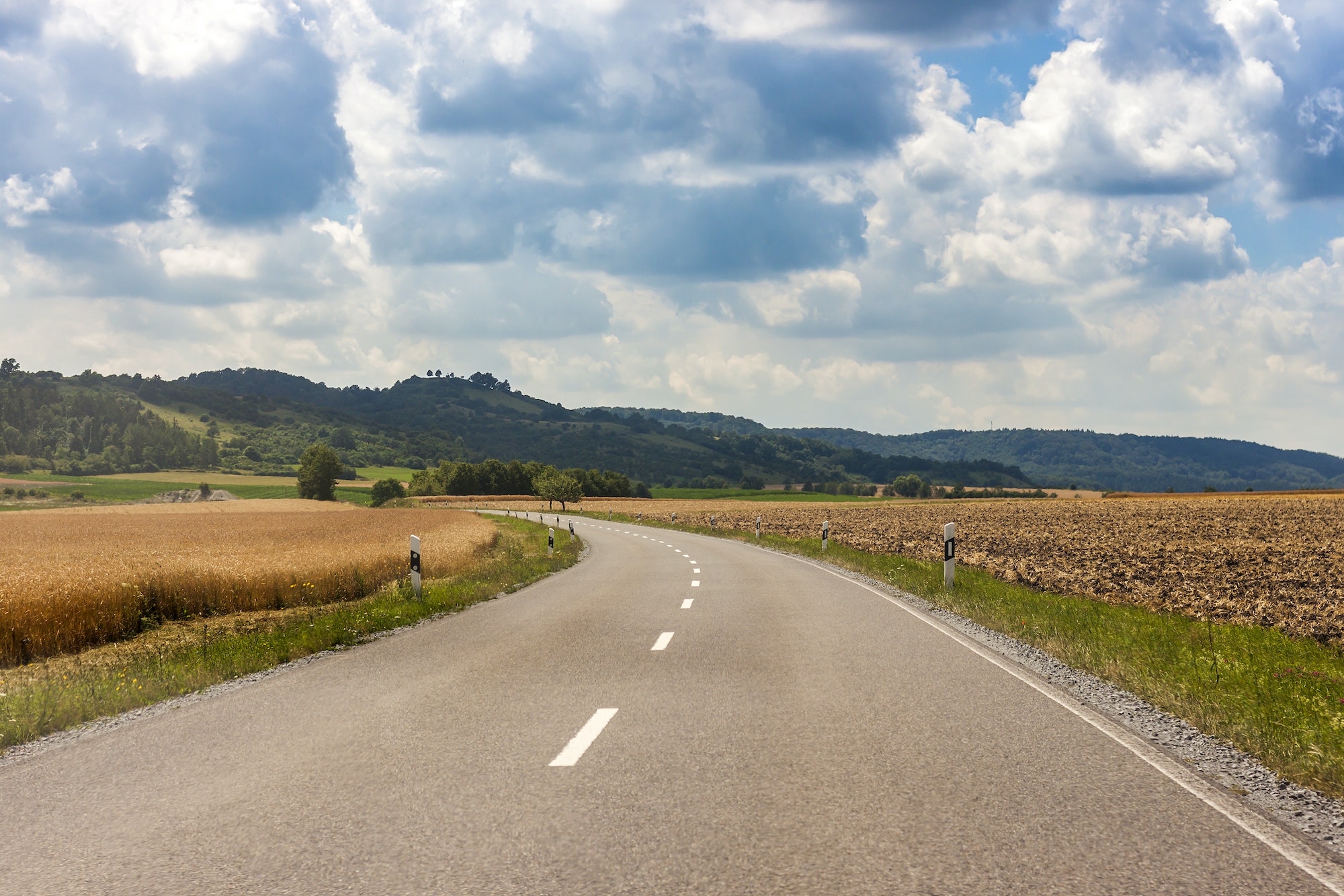 Asphalt country rural road in Germany through the green field and clouds on blue sky in summer day
