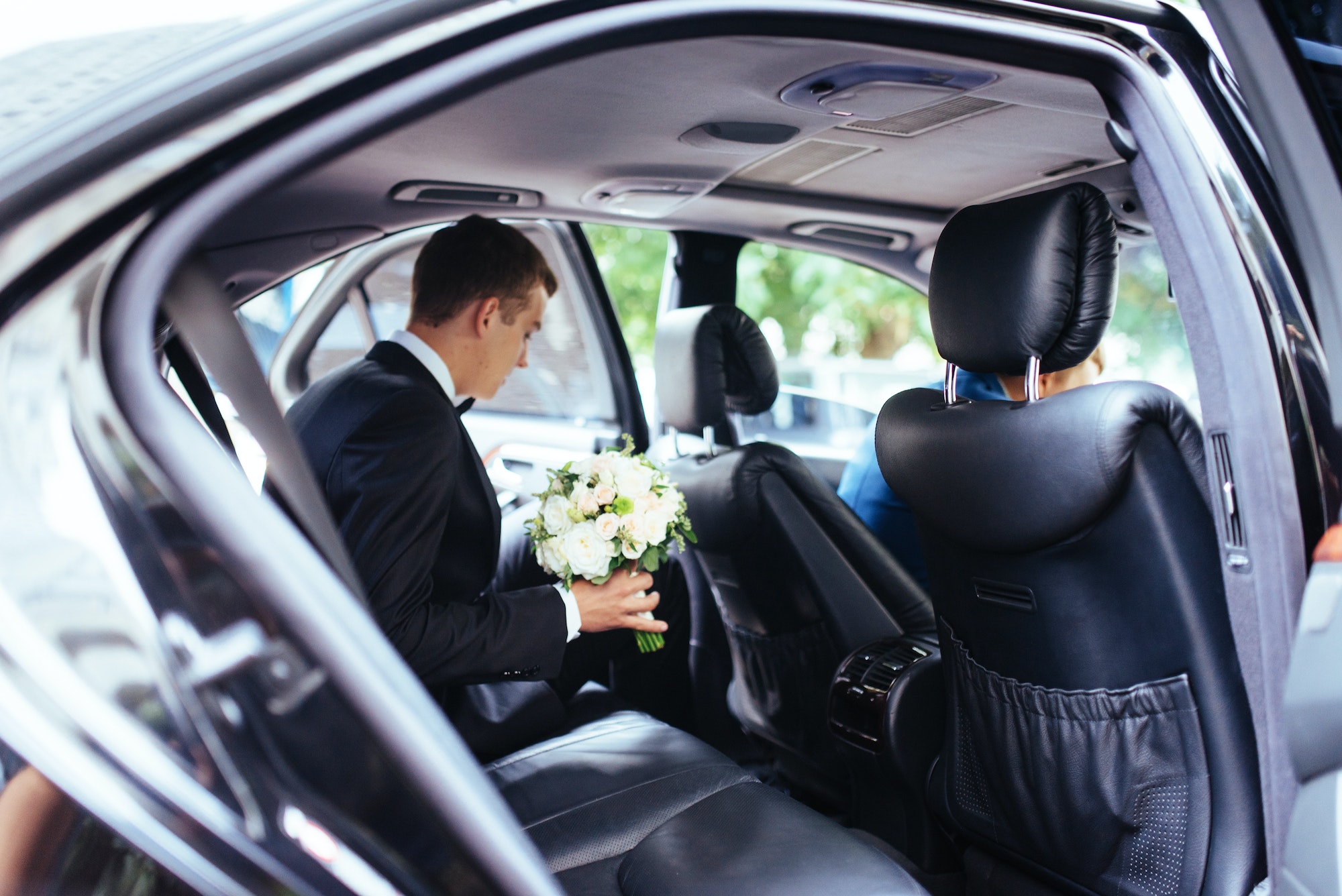 Happy beautiful bride, sitting in wedding car with a bouquet